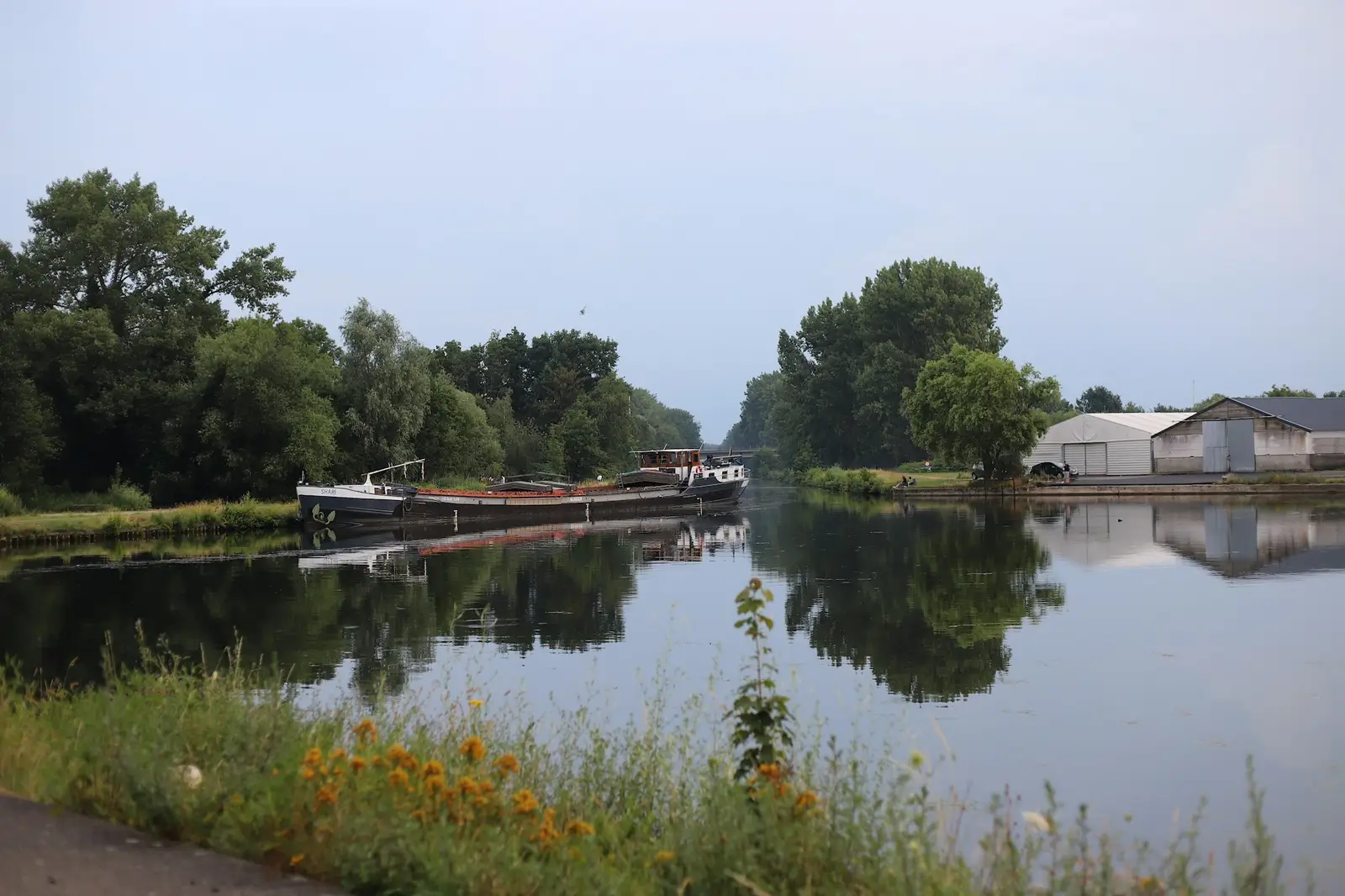 Rivière bordée d’arbres, une péniche à quai