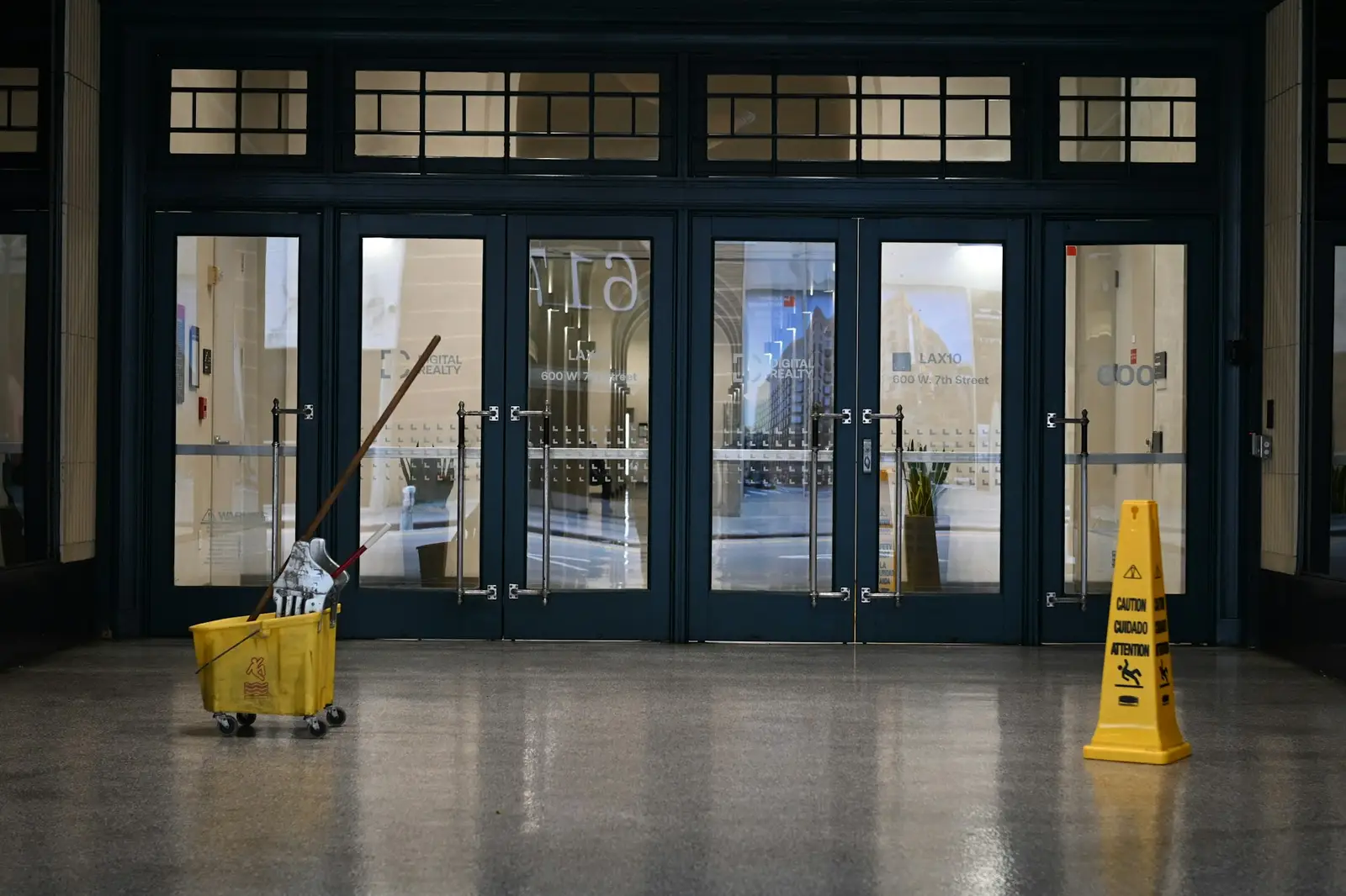 Seau et panneau « sol glissant » devant des portes vitrées